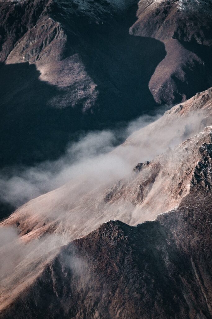 Misty rugged mountain slopes with rocky textures and dramatic shadows in earthy tones wallpaper