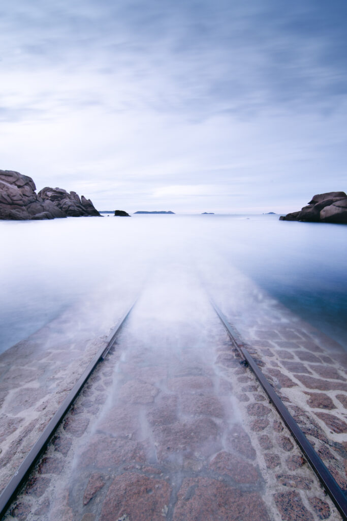 Old rusty rails fading into misty water with smooth stones and soft blue pastel tones wallpaper