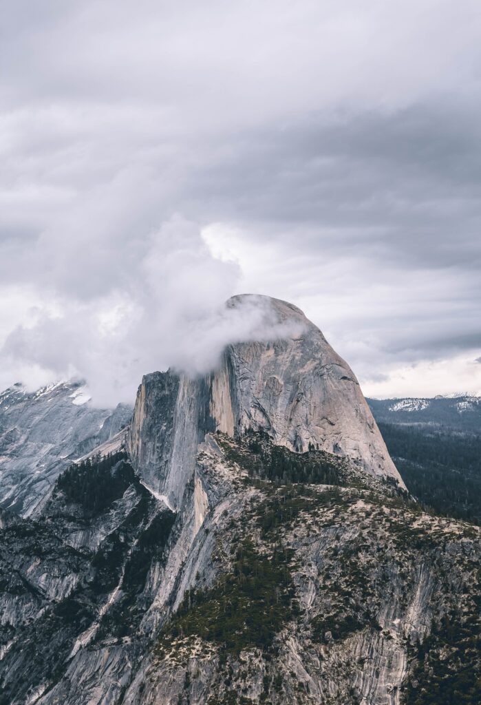 Misty rugged rock cliff with steep slopes above dense green forest cool muted nature wallpaper