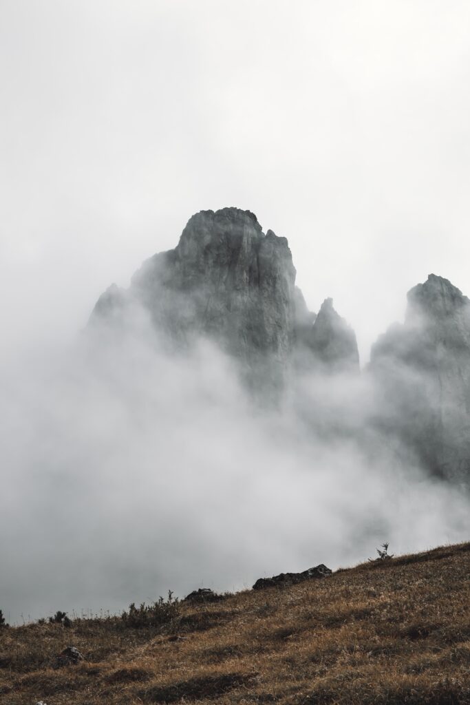 Foggy rocky mountains with grassy slope in foreground dramatic landscape wallpaper background