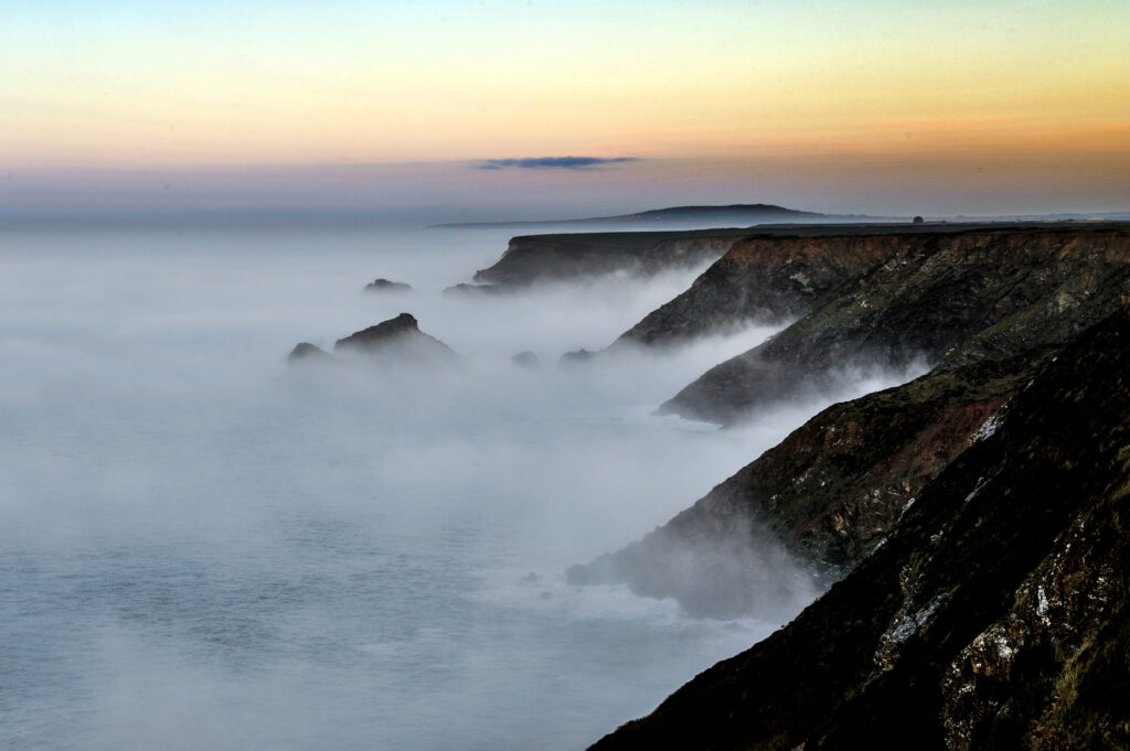 Rugged coastline with sea cliffs in morning fog under soft dusk sky tranquil coastal wallpaper