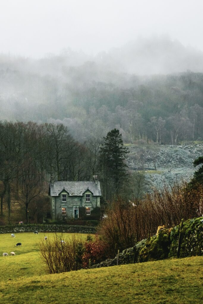 Charming rural house in misty landscape with lush grass grazing sheep and distant foggy hills Wallpaper