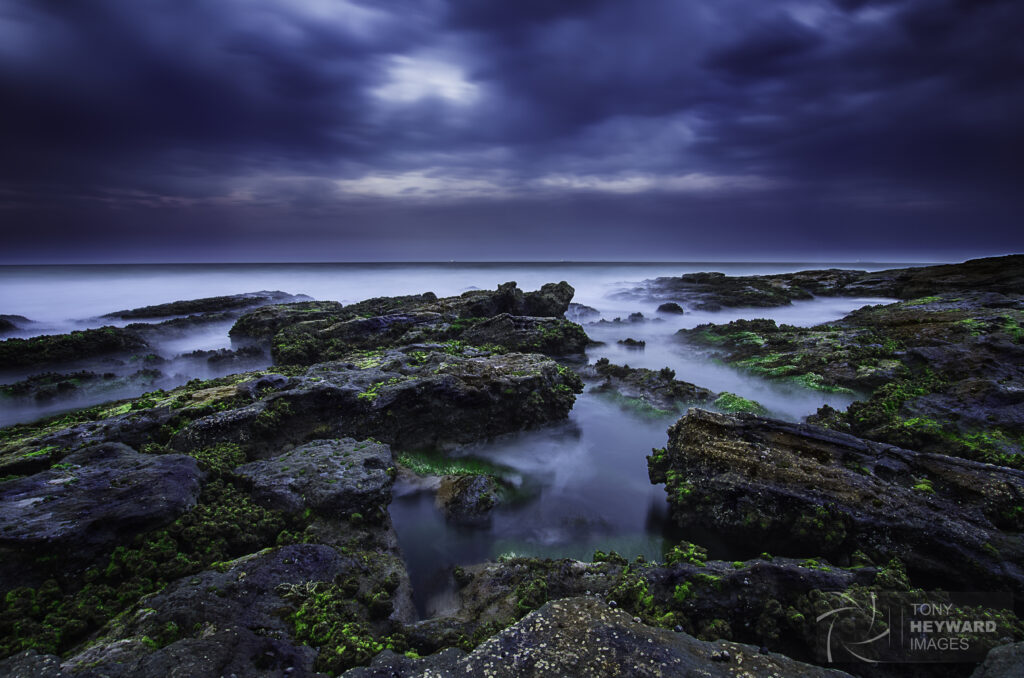 Misty seashore with rugged stones and vibrant moss under moody cloudy sky wallpaper background