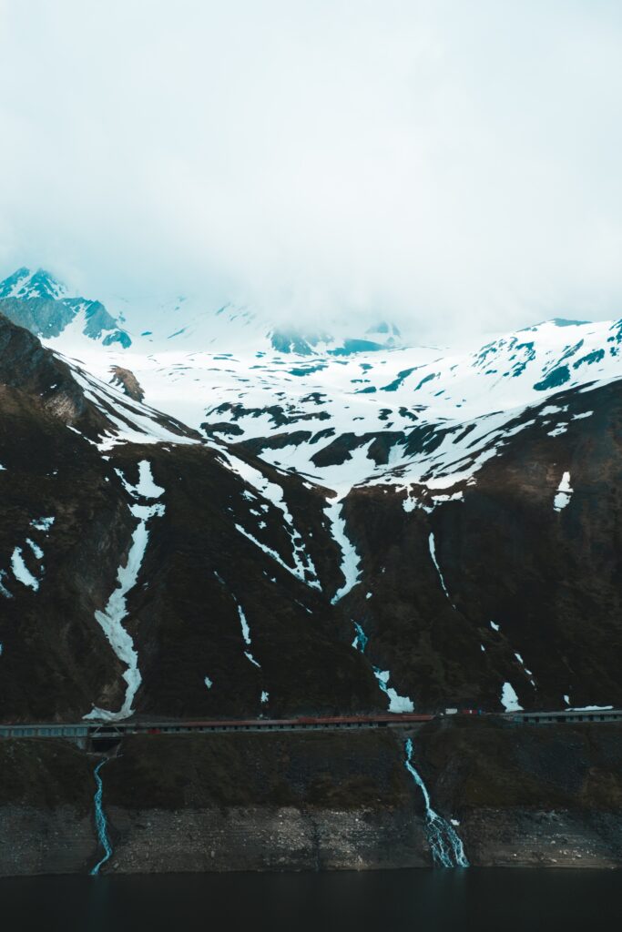 Snow-covered rugged mountains with jagged cliffs and misty clouds in a serene wilderness wallpaper