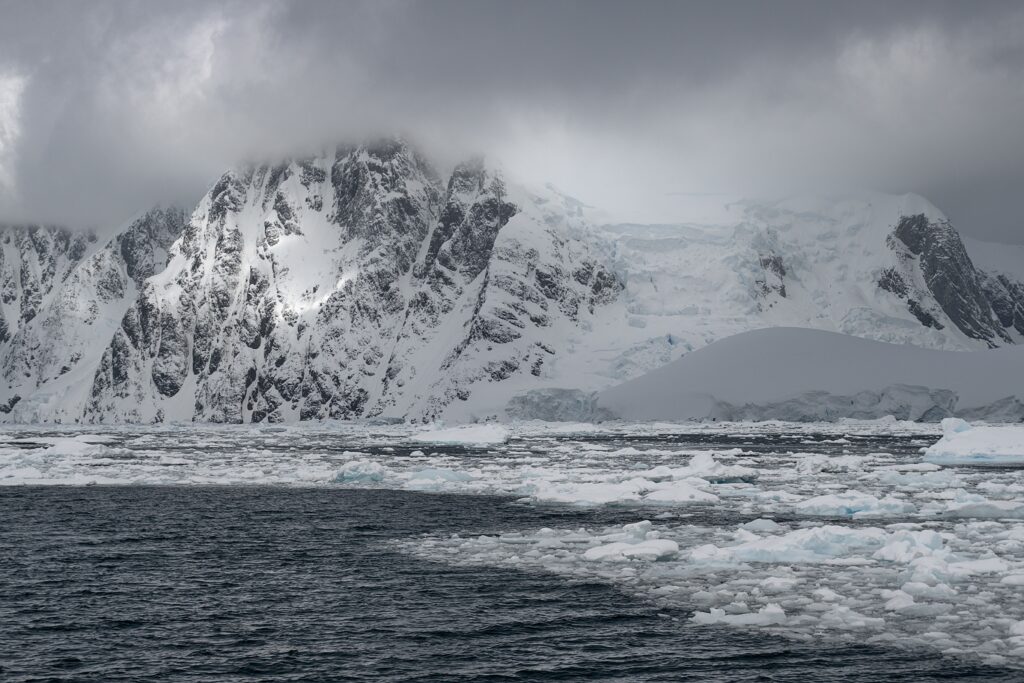 Snowy mountains misty landscape with dark sea and floating ice in a remote cold region wallpaper
