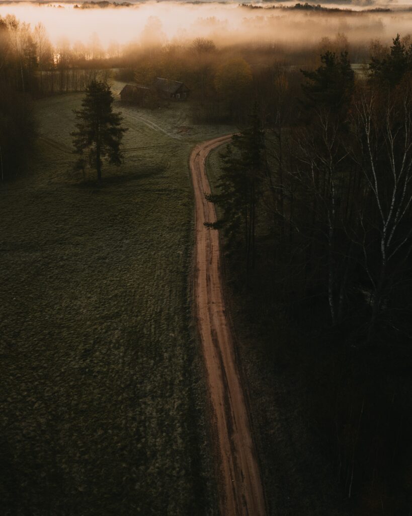 Aerial view of winding road through misty field and trees at sunset golden light rural landscape Wallpaper