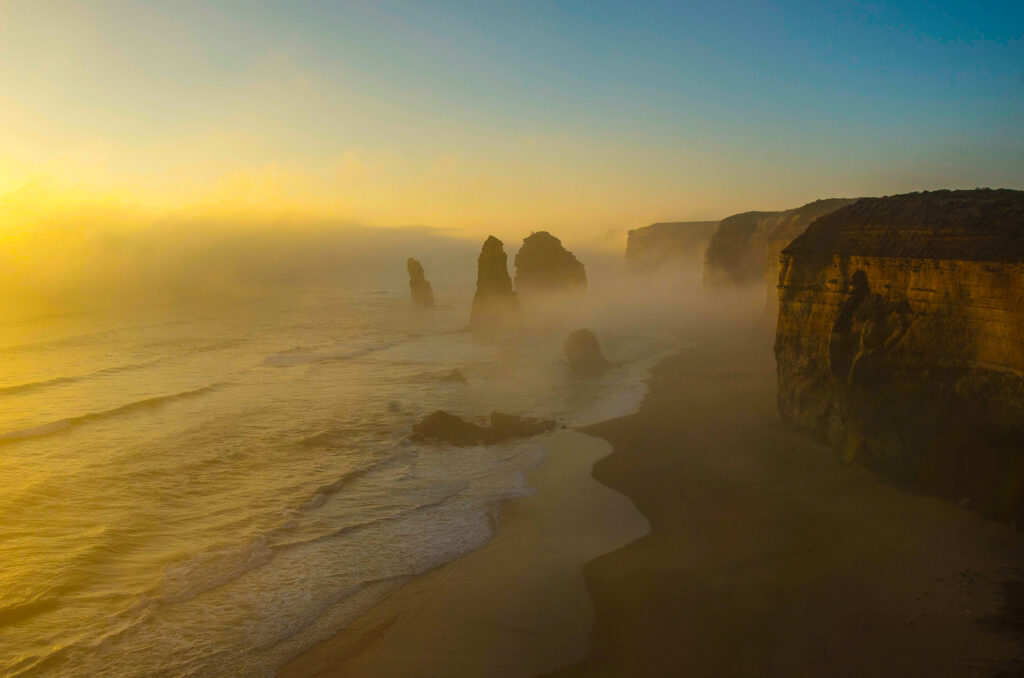 Foggy twilight coastal rocks with golden sunlight and serene waves creating moody seascape Wallpaper