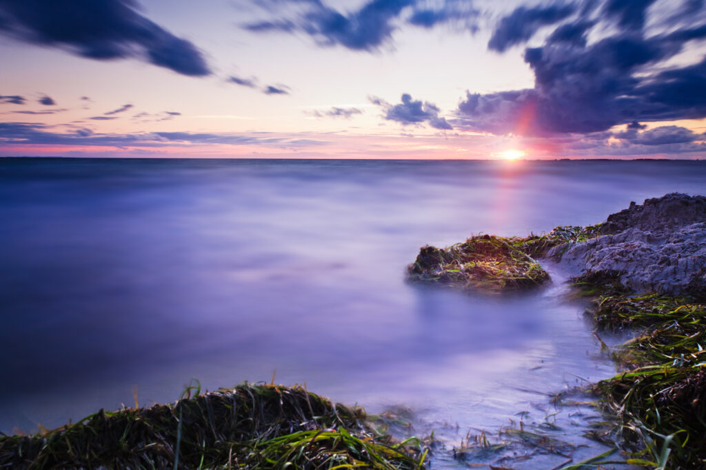 Misty twilight coastal wallpaper with gentle waves grassy rocks warm sunset and dramatic clouds