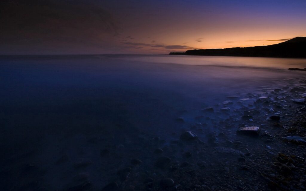 Misty coastline at twilight with smooth stones and soft foggy water under vibrant sky wallpaper