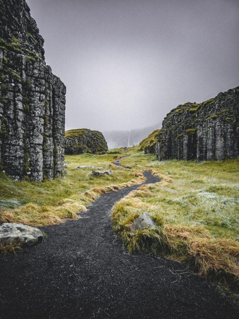 Winding path through misty valley with towering rock formations and lush green moss landscape Wallpaper