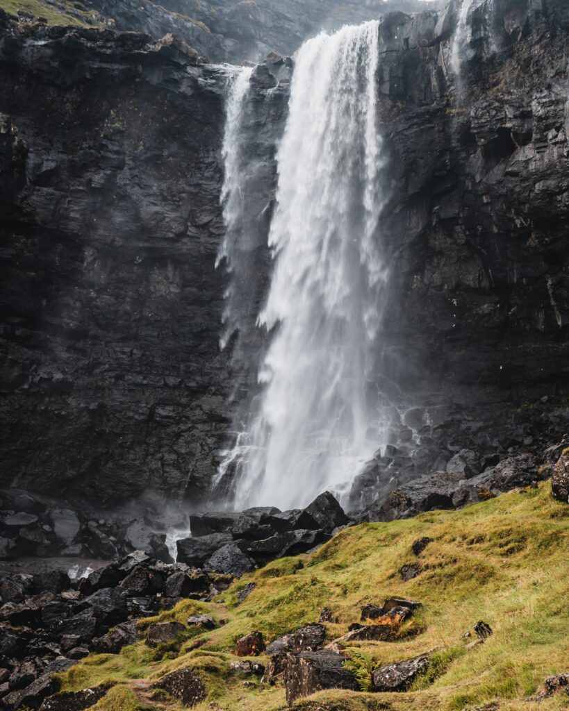 Powerful waterfall cascading over dark rocks with mist and green moss in natural landscape wallpaper