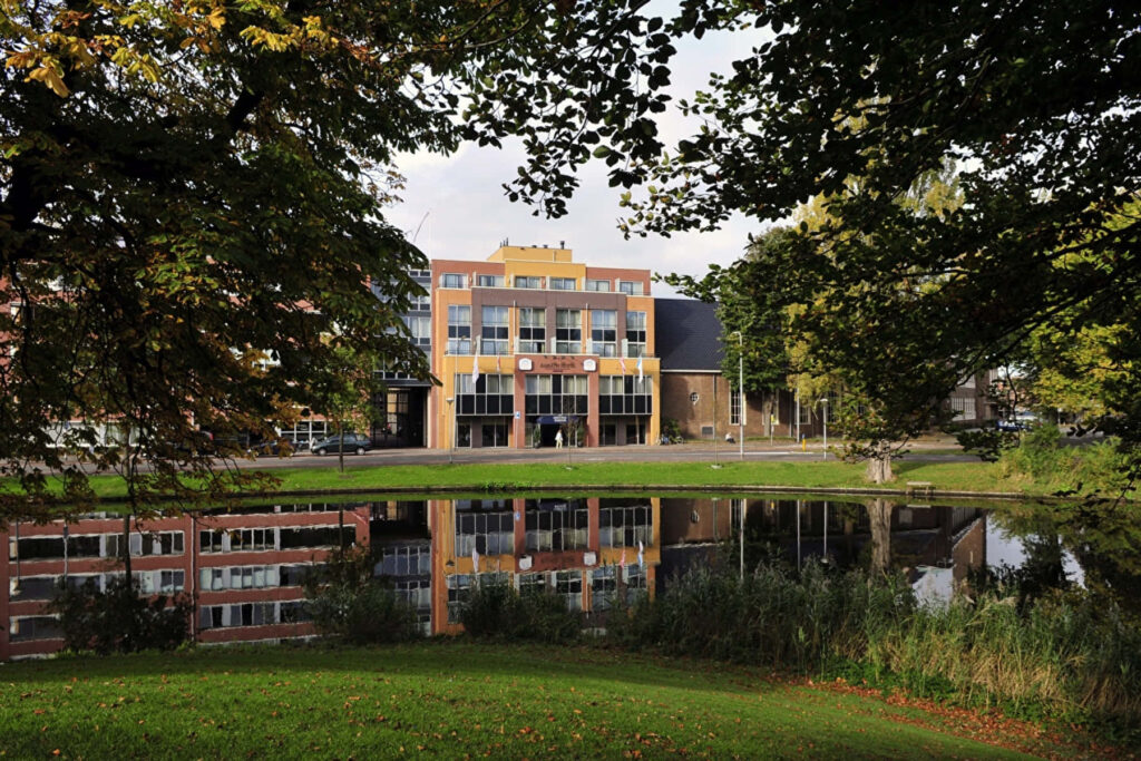Modern building in Alkmaar reflected in calm water surrounded by green trees and lawn wallpaper