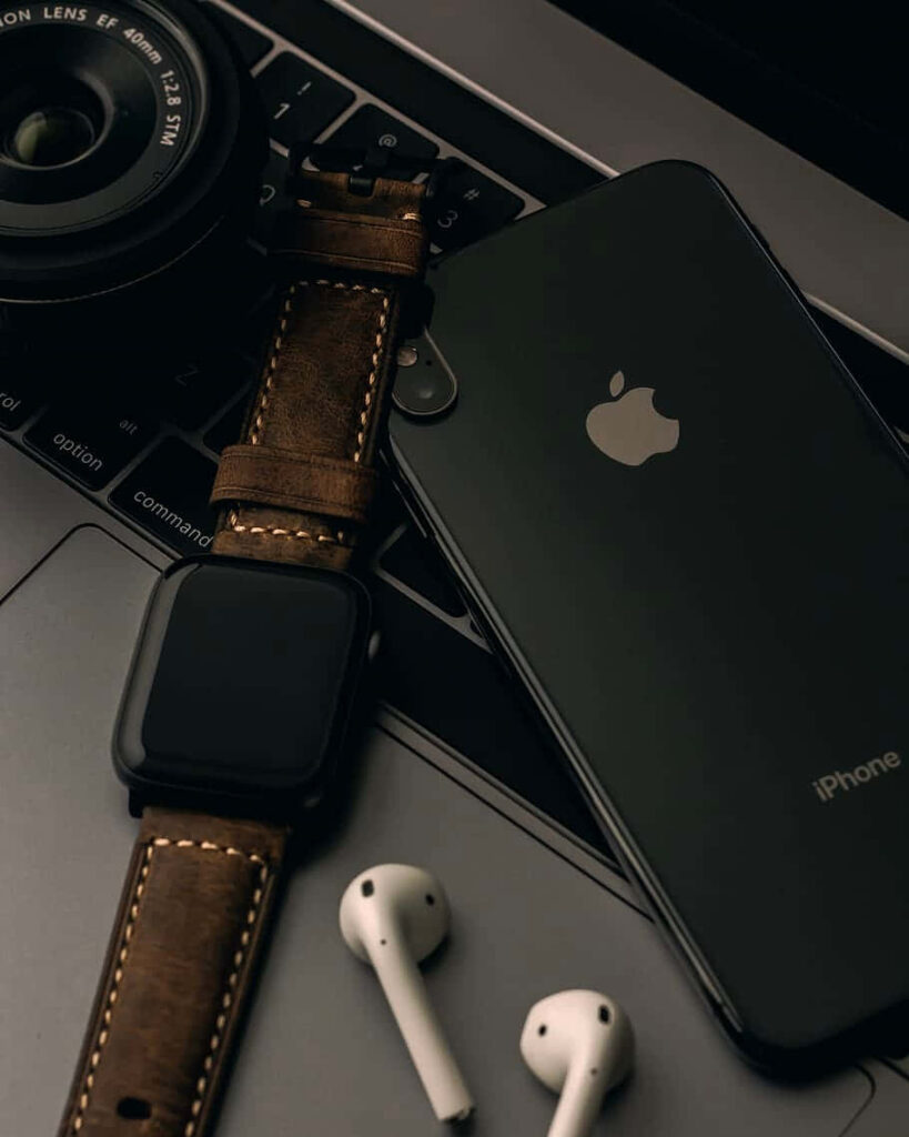 Flat lay of Apple iPhone X AirPods Apple Watch with leather band on laptop showcasing tech essentials Wallpaper