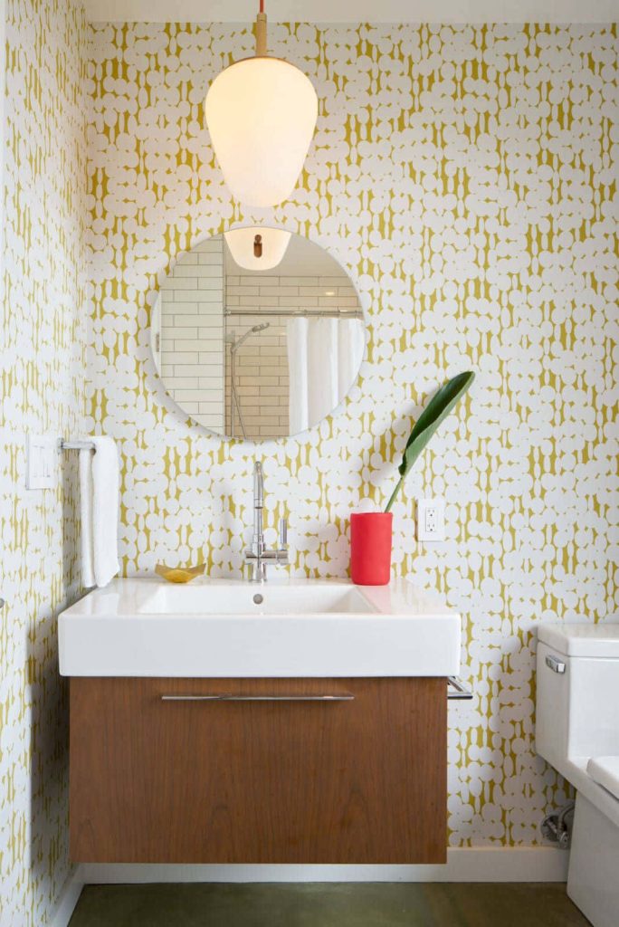 Modern bathroom with floating wood vanity white sink yellow patterned wallpaper and red vase