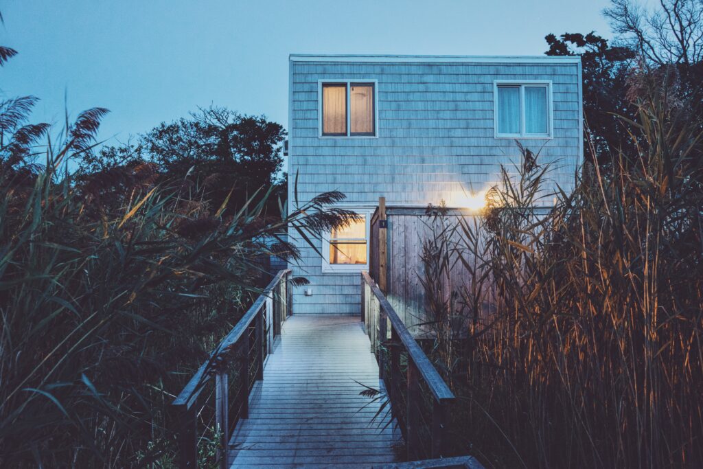 Modern box-shaped building lit by warm lights surrounded by tall grass at dusk wallpaper background
