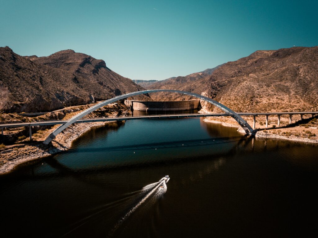 Modern bridge over calm sea with rugged mountains and boat under vivid blue sky wallpaper