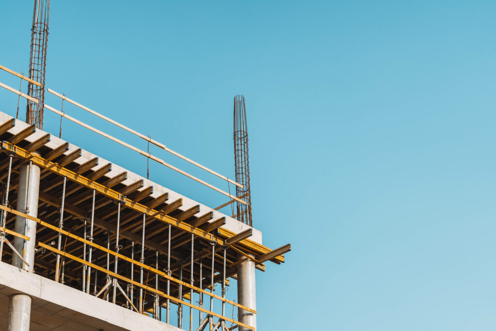 Modern building construction with concrete columns steel bars and yellow framework under blue sky Wallpaper
