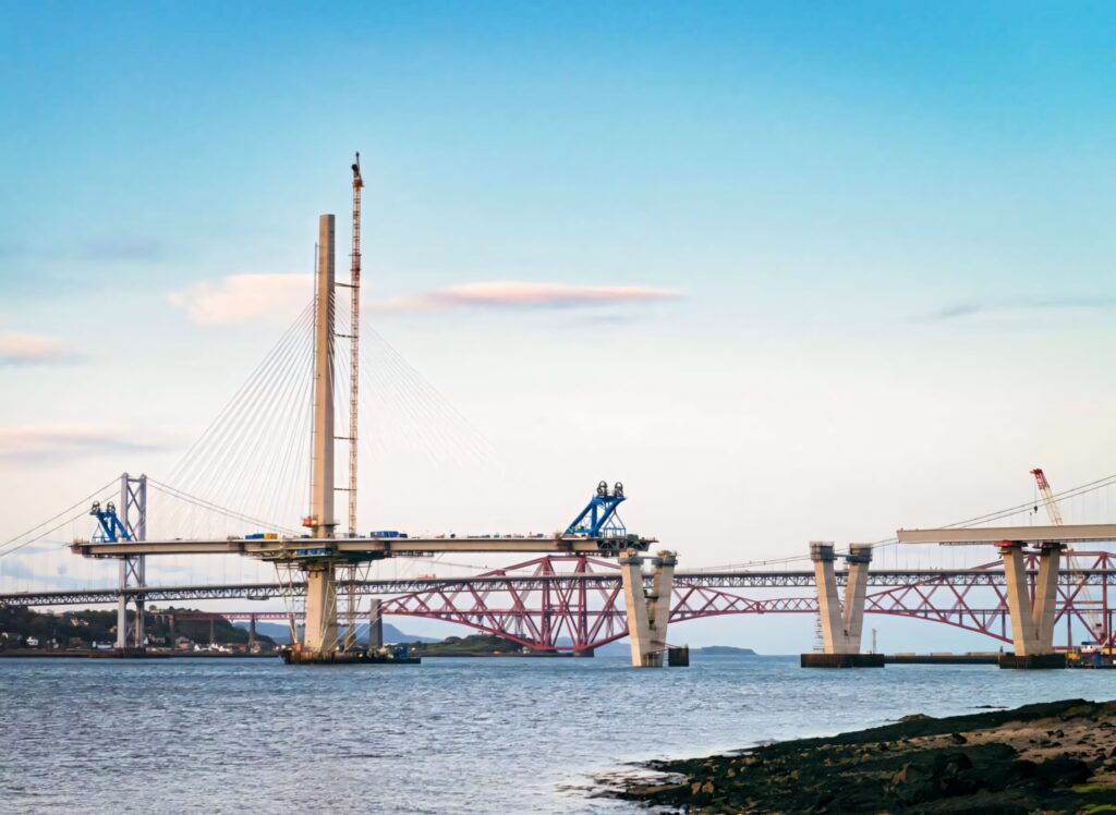 Modern cable stayed bridge construction with cranes steel framework and towering pylons over river Wallpaper