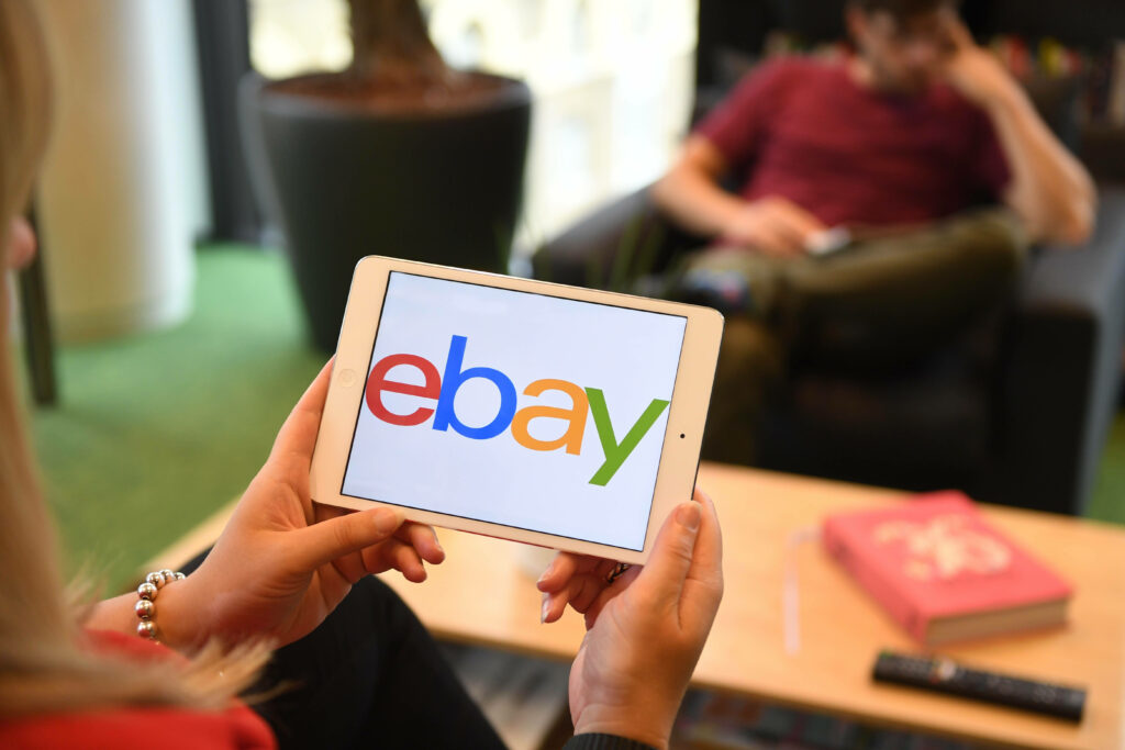 Person holding tablet showing colorful eBay logo in modern indoor setting for online shopping Wallpaper