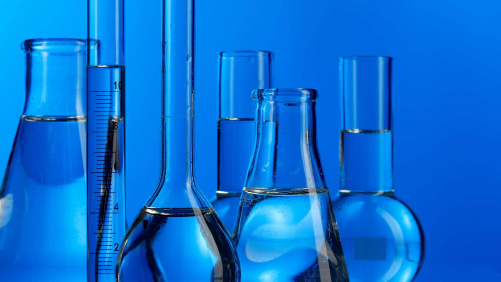 Glass laboratory beakers and cylinders with clear liquid on vivid blue background scientific wallpaper