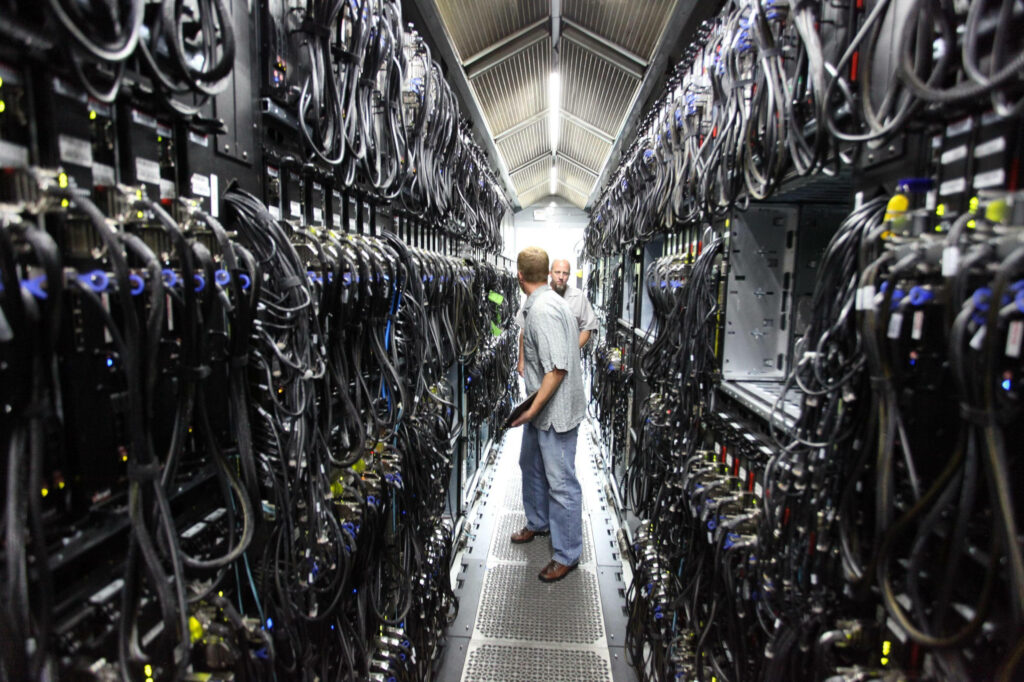 Modern data center with organized black cables and technicians maintaining server racks under bright lights Wallpaper