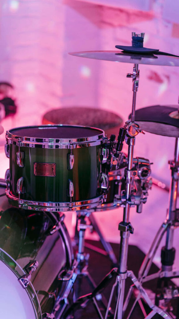 Close-up of modern drum set with chrome hardware and deep green finish under colorful lights Wallpaper