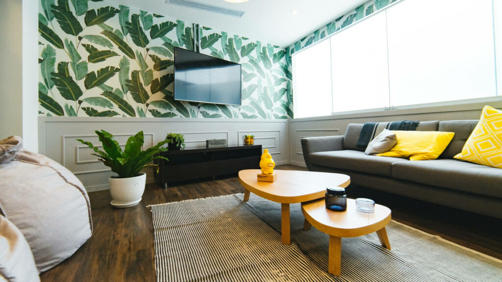 Modern workspace with tropical palm leaf wallpaper cozy grey sofa yellow accents wooden tables
