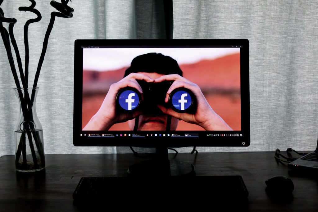 Person using binoculars with Facebook logos on lenses on computer screen modern social media wallpaper