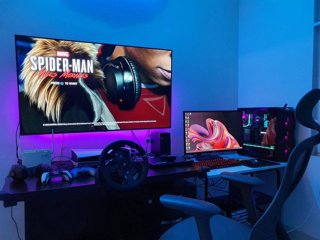 Modern gaming room with Marvel Spider-Man screen blue lights PC tower racing wheel setup Wallpaper