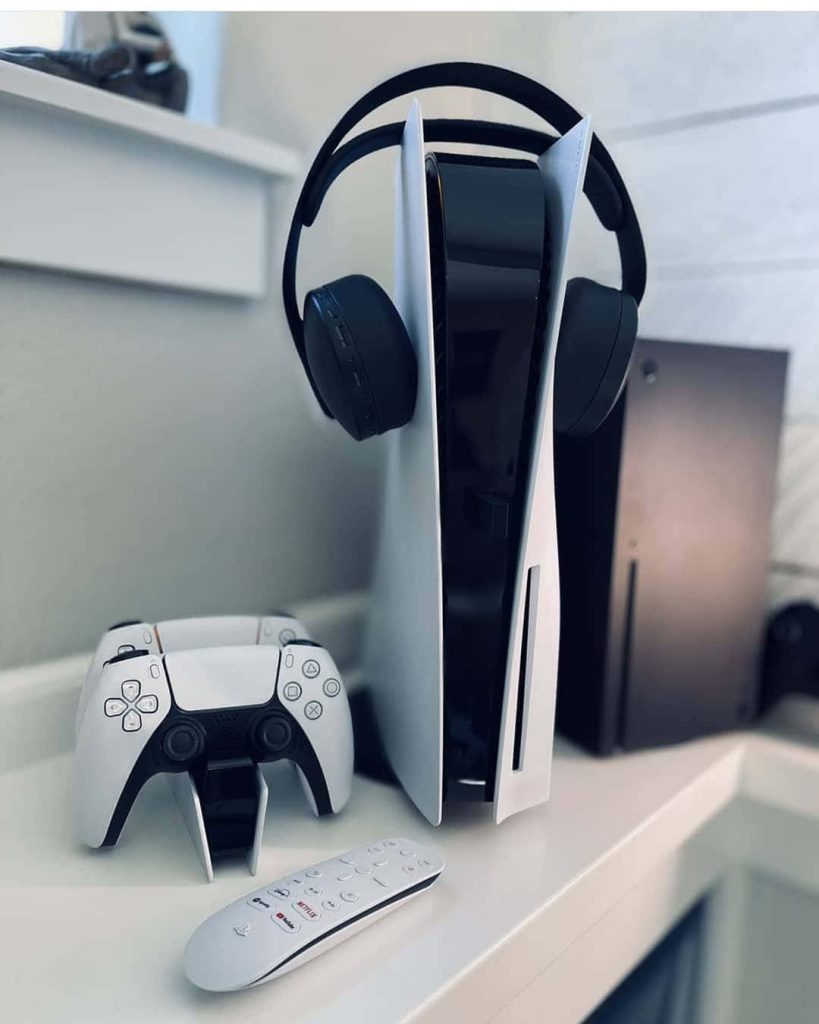 Clean gaming setup wallpaper with Sony PS5, DualSense controller, headphones, Xbox Series X background
