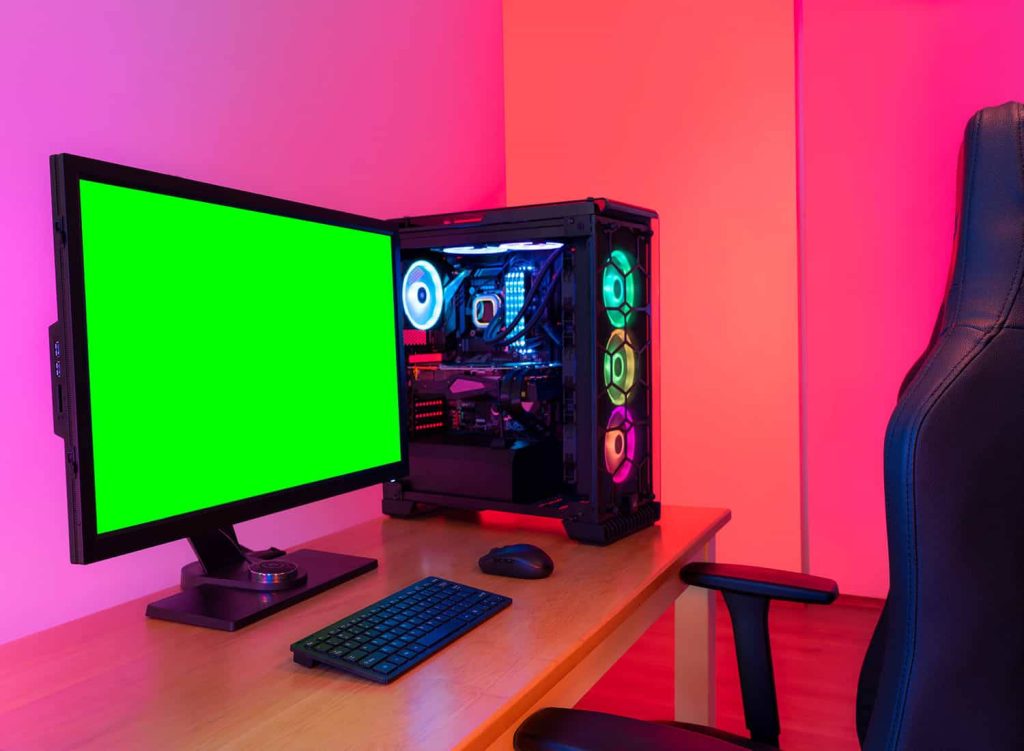 Modern gaming setup with RGB PC tower green screen monitor neon pink ambient lighting desk Wallpaper