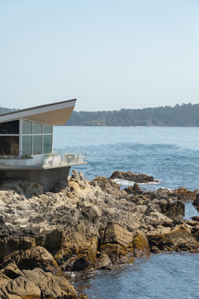 Modern glass building on rocky coast overlooking calm blue sea and distant shoreline clear sky wallpaper