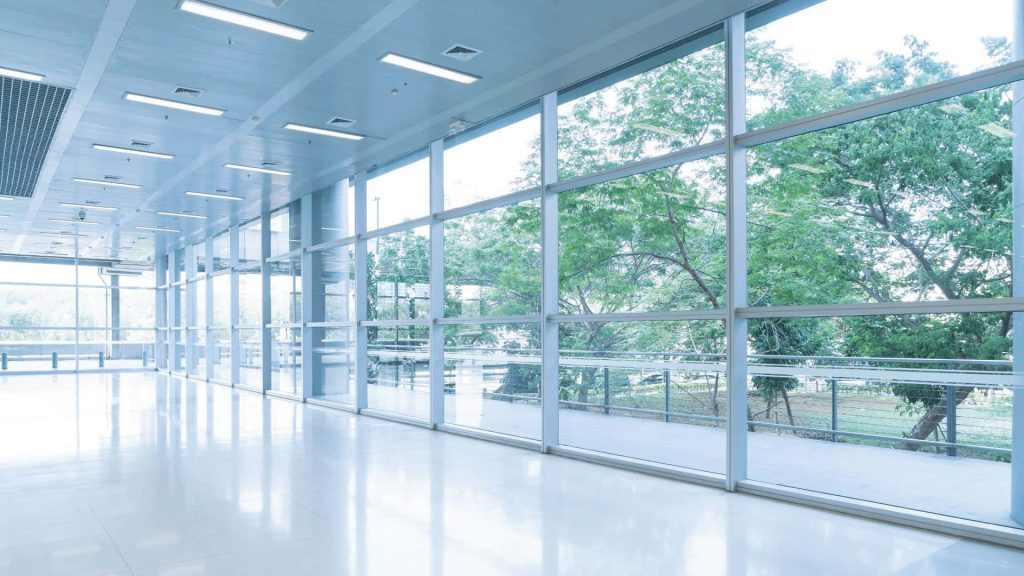 Modern glass hallway with bright floors and large windows overlooking green trees office background Wallpaper