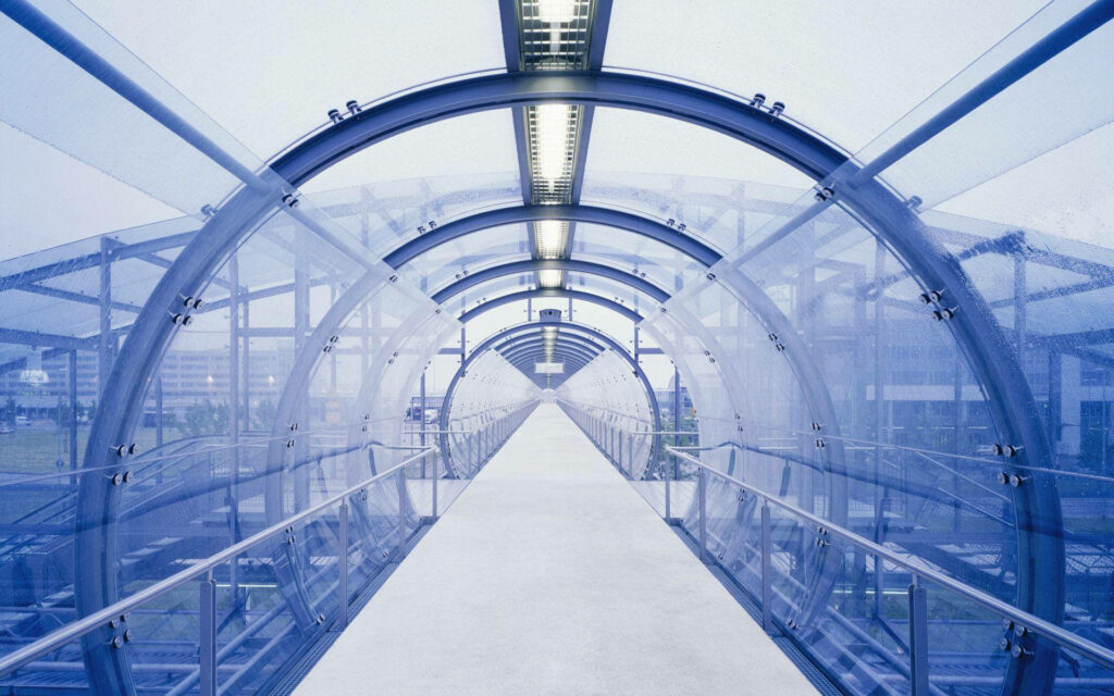 Transparent glass tunnel bridge with blue steel framework bright lighting modern engineering design Wallpaper