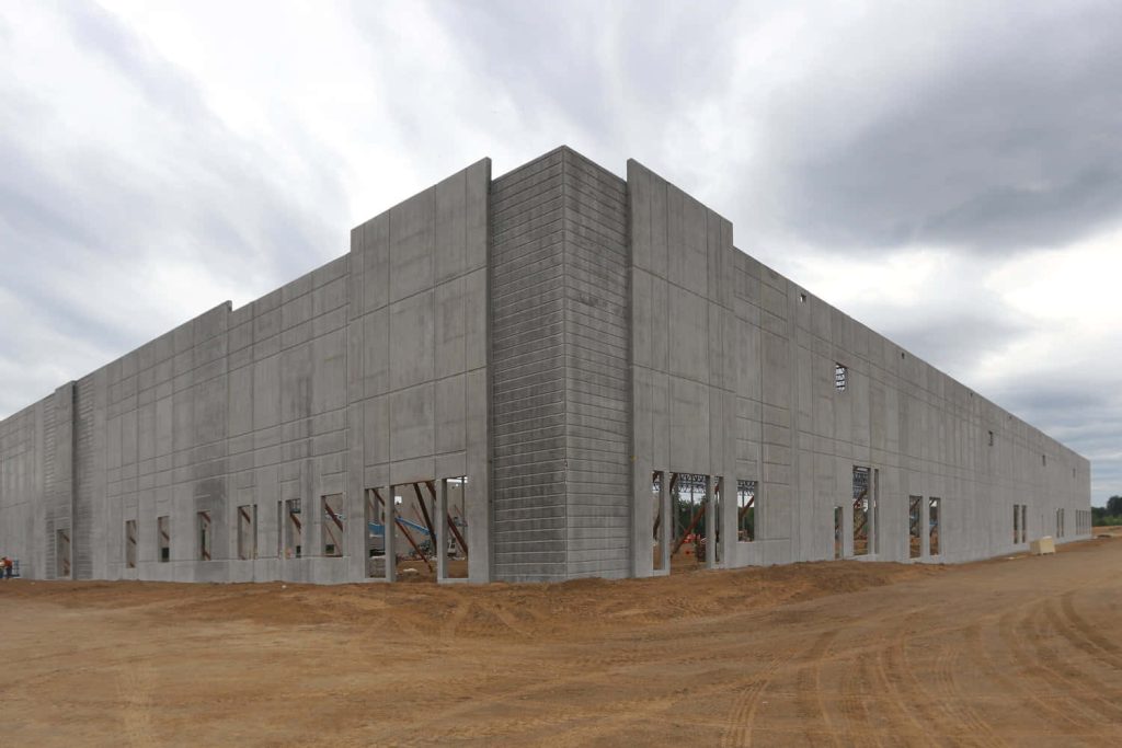 Large industrial building under construction with grey precast concrete panels and dirt site Wallpaper