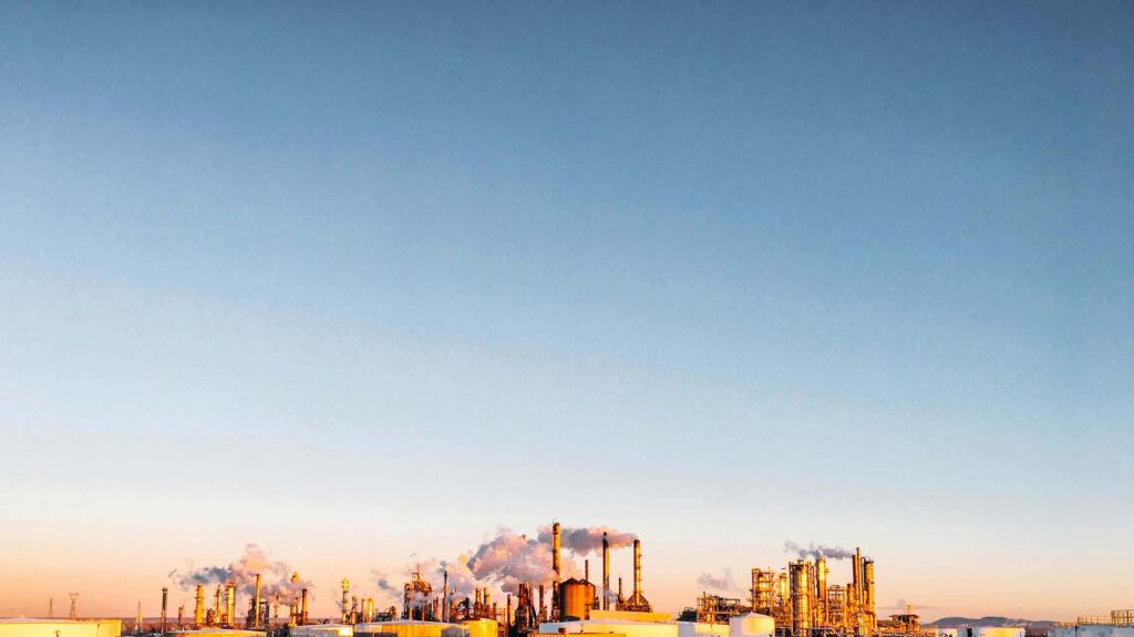 Modern factory complex with smokestacks under blue sky golden sunlight highlights industrial scale Wallpaper