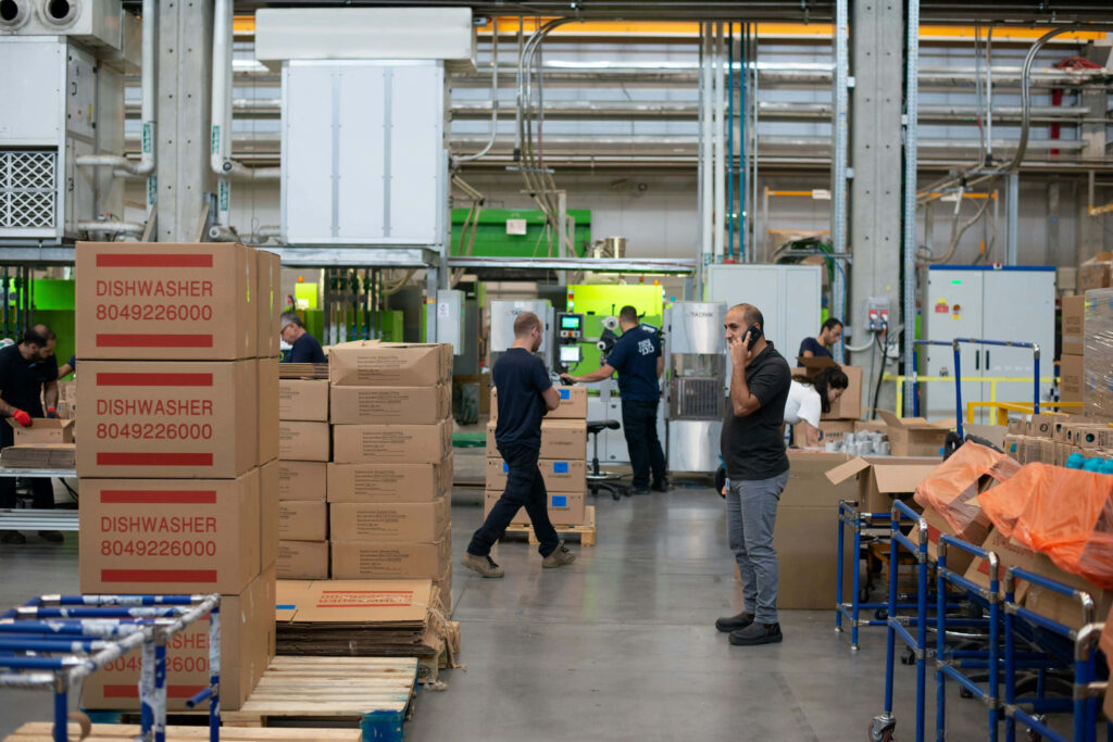 Modern factory warehouse with workers handling boxes conveyors shelves and bright lighting Wallpaper