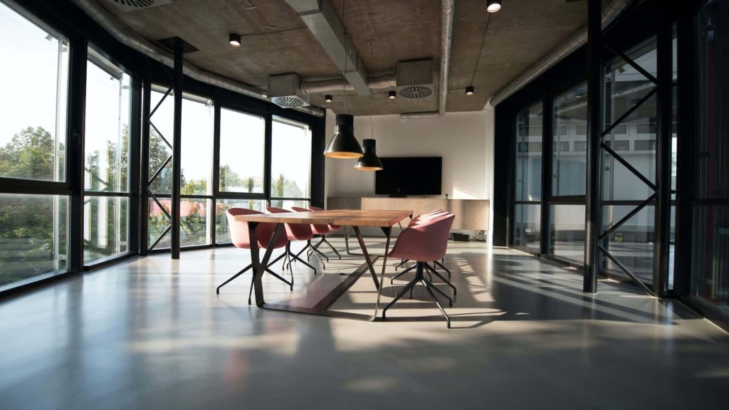 Modern industrial Zoom office background with wooden table pink chairs and glass walls Wallpaper