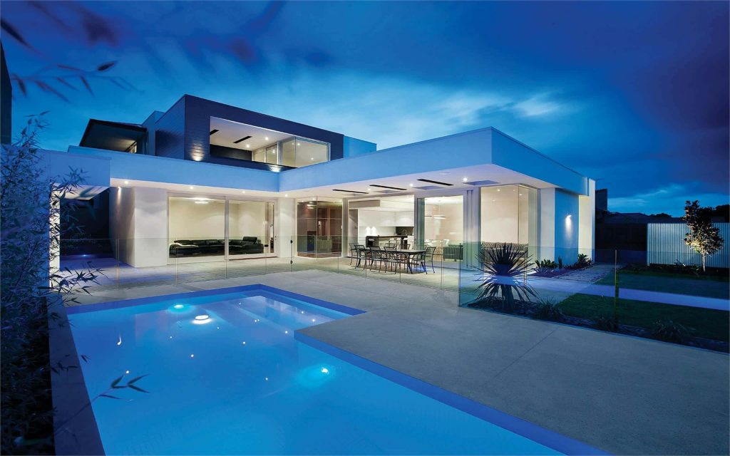 Modern luxury home with glowing glass walls and a serene pool reflecting twilight sky wallpaper