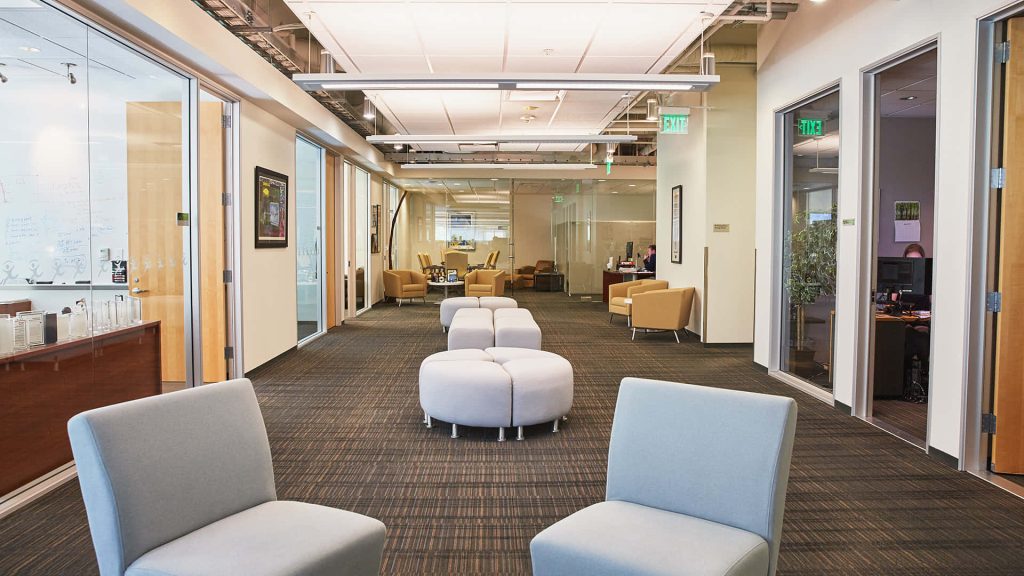 Modern office corridor with glass meeting rooms and light grey lounge chairs background wallpaper