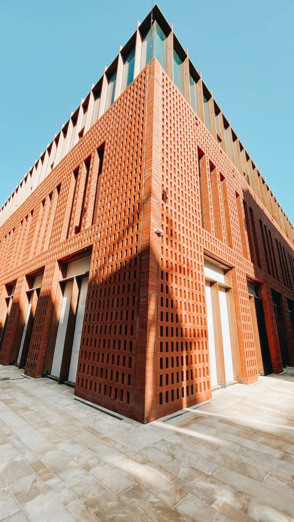 Low-angle view of modern red brick lattice building with sharp shadows under clear blue sky wallpaper