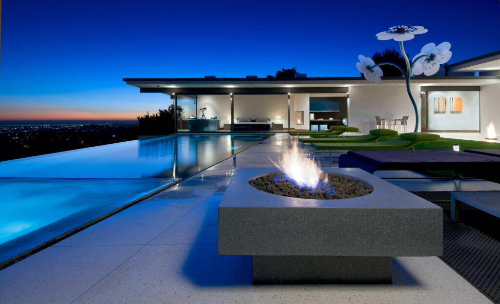 Luxurious California villa at twilight with infinity pool fire pit green loungers and sculpture Wallpaper