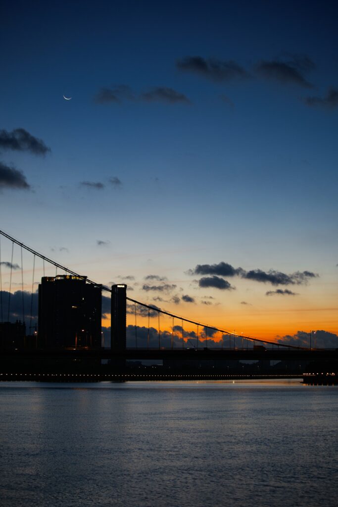 Modern bridge over calm water with city skyline at vibrant orange and blue sunset sky Wallpaper