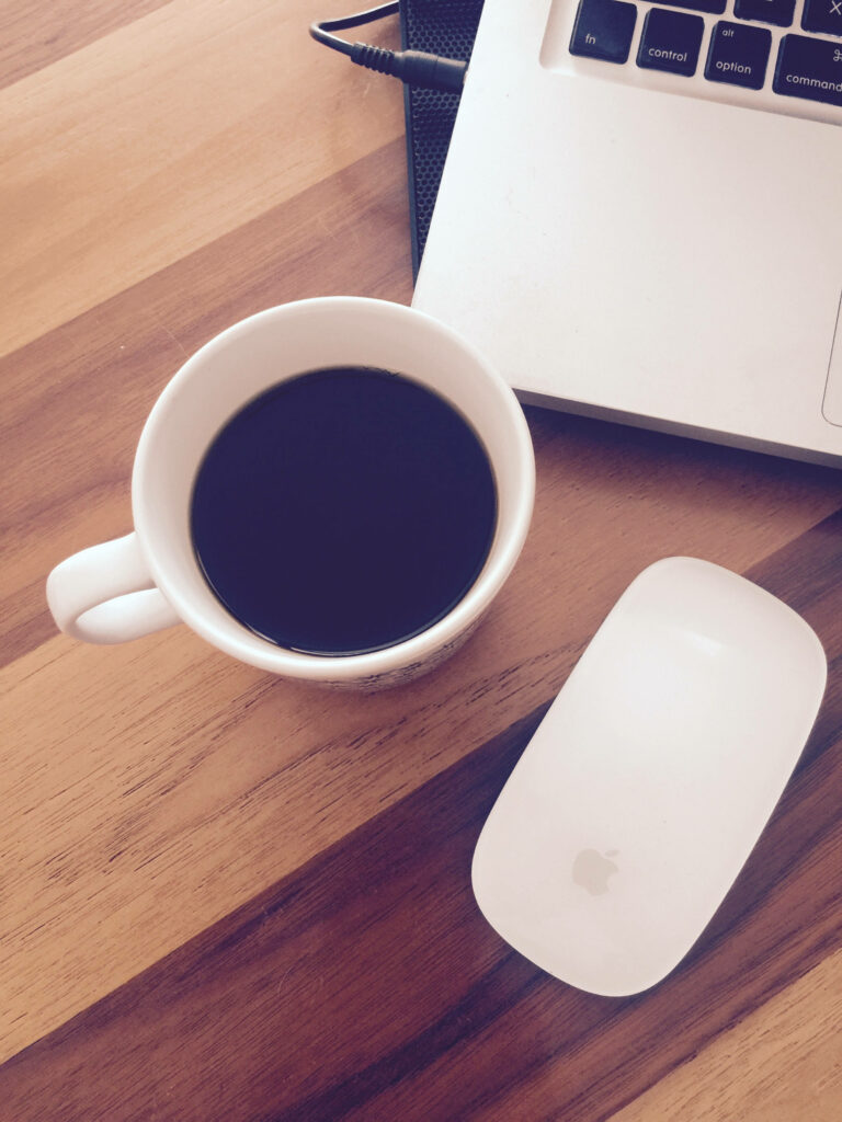Stylish workspace with Apple Magic Mouse laptop and steaming black coffee on wooden desk Wallpaper