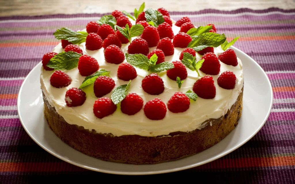 Moist cake with creamy frosting fresh raspberries and mint leaves vibrant dessert wallpaper background