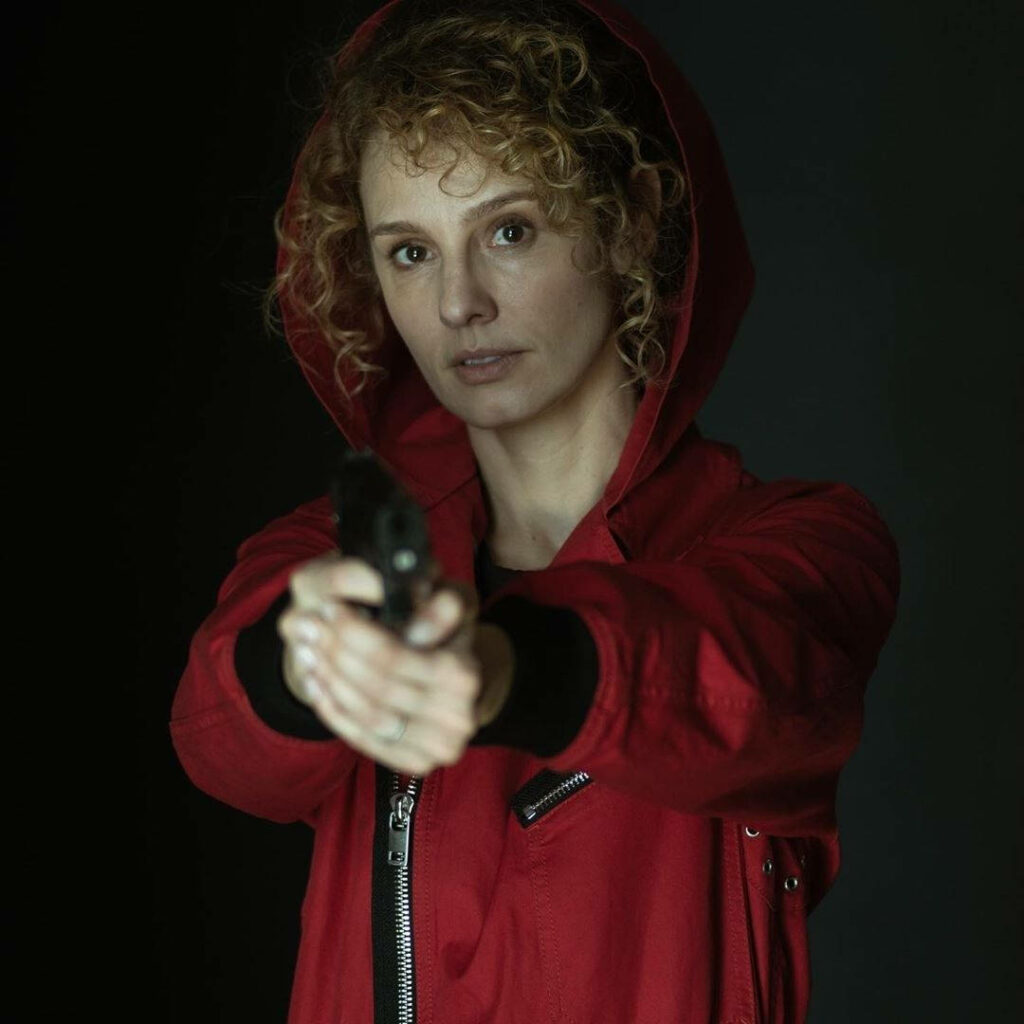 Monica's Intense Stare: Money Heist's Fearless Gun-Wielding Heroine Strikes a Bold Pose Against the Shadows Wallpaper