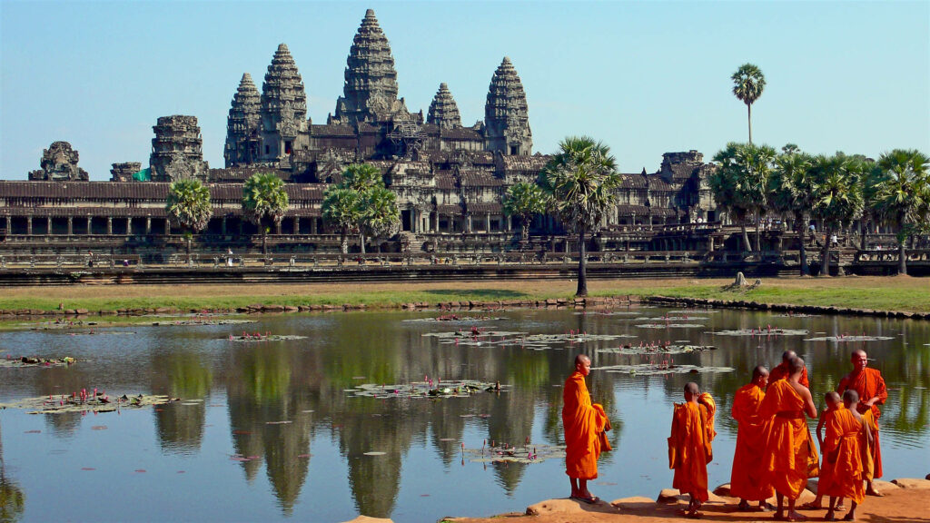 Monks in orange robes by pond with Angkor Wat temple and clear blue sky scenic wallpaper background