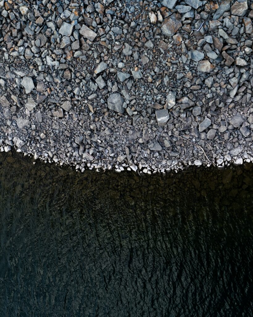 Aerial view of rugged rocky coastline meeting calm dark water in minimalist monochrome tones wallpaper