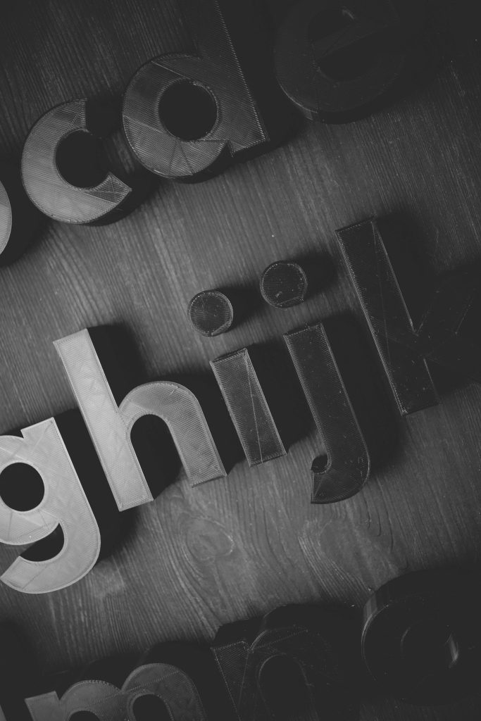 Close up of black 3D printed lowercase letters on dark textured surface with dramatic lighting Wallpaper