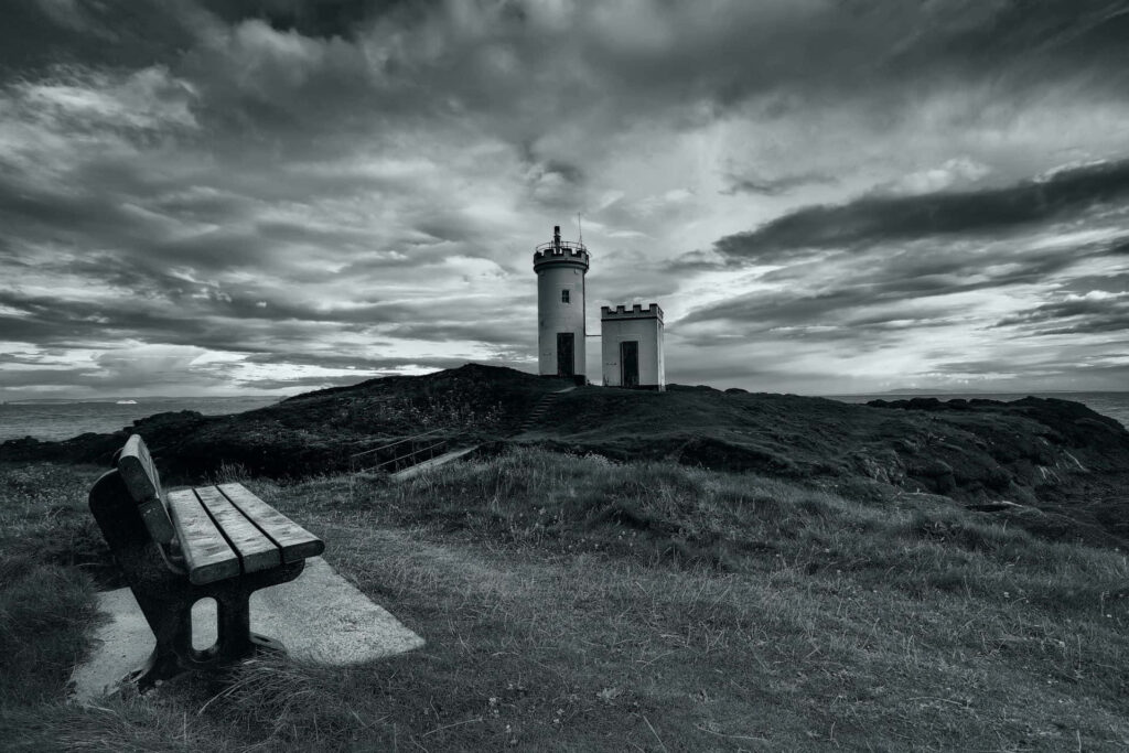 Serene Coastal Landscape: Monochrome Lighthouse and Rustic Bench Wallpaper